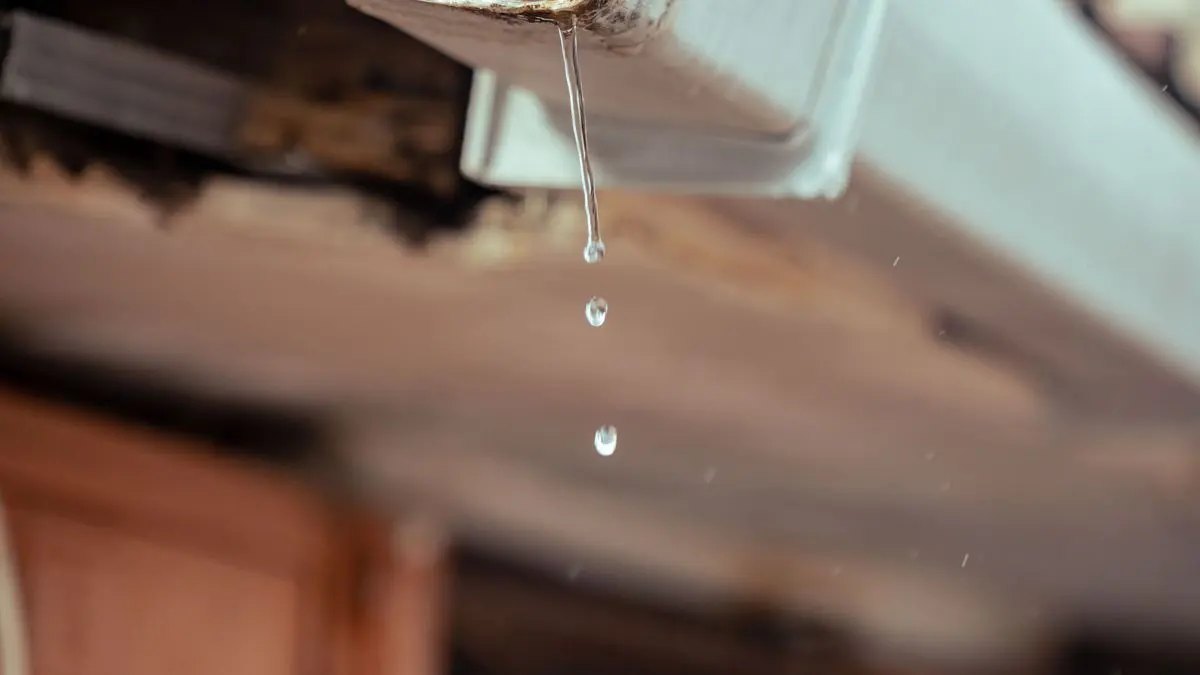 Gotas de agua que caen del borde de una canaleta blanca, vista desde abajo