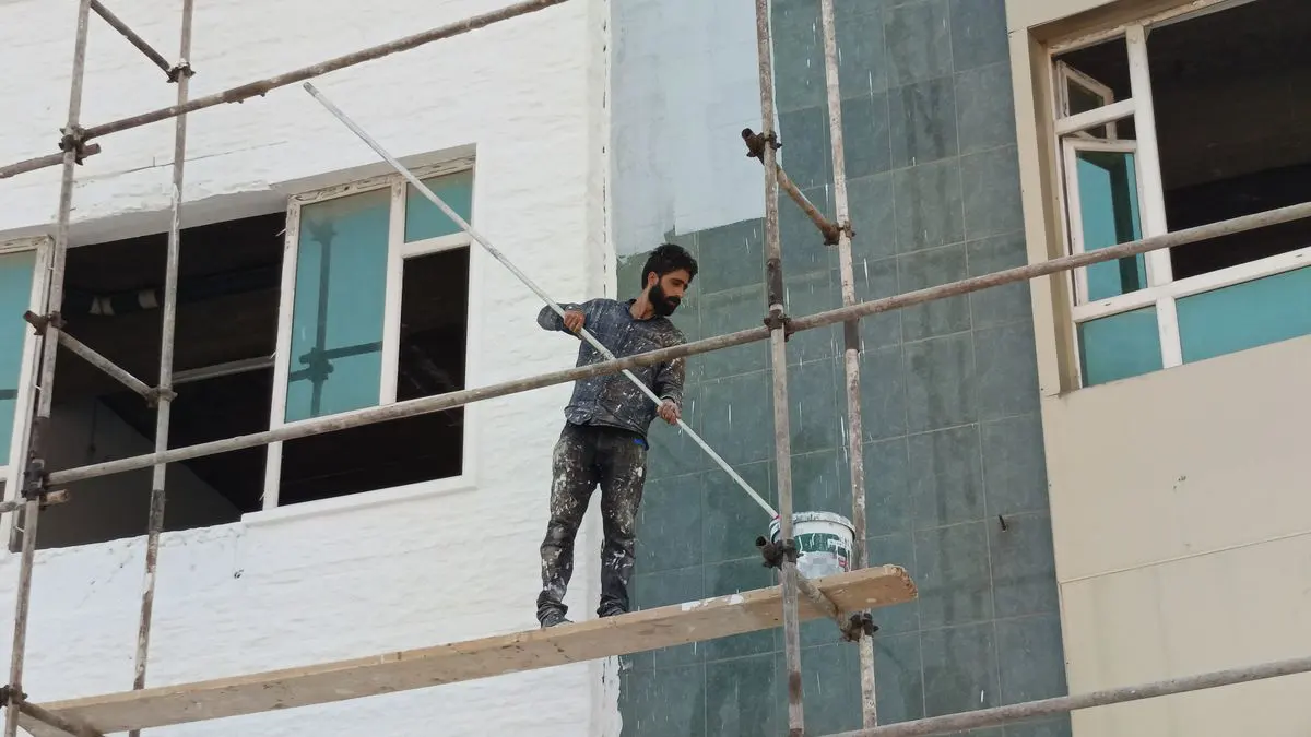 Operario en un andamio pintando con rodillo la fachada de un edificio