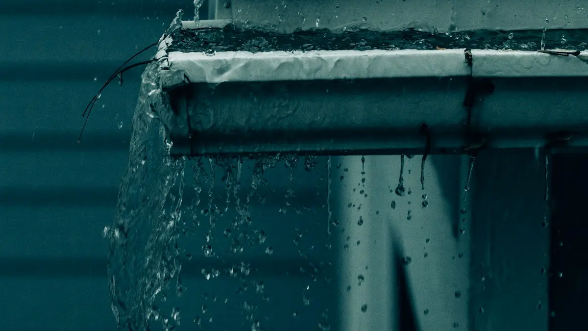 Canaleta llena de agua que desborda durante la lluvia, junto a una pared