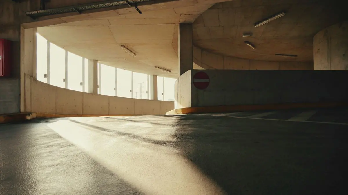 Rampa curva de un garaje de hormigón con piso oscuro y luz entrando por los ventanales